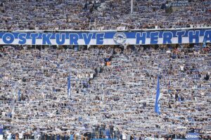 Hertha-Fans im Stadion, Emotionen sichtbar, während Sicherheitskräfte und Stadionatmosphäre prävalieren.