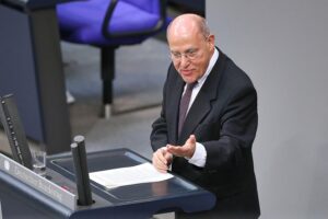 Ein Porträt von Gregor Gysi, umgeben von symbolischen Elementen zu Justiz und Demokratie.