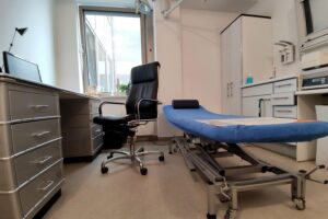 Behandlungszimmer mit Ärzten und wartenden Patienten, symbolisiert die Debatte um Telefon-Krankschreibung.