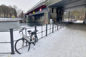 Schneebedeckte Berliner Straße, Protest für Obdachlosenunterkünfte, winterliche Kälte, menschenleere Bürogebäude.
