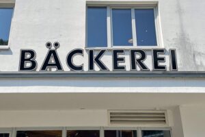 Bäckerei mit gespannten Angestellten und ruhiger Atmosphäre, während Polizei eintreffen könnte.