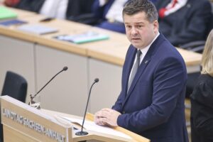 Sven Schulze spricht in der Landtagssitzung, umgeben von politischen Symbolen und Debattenatmosphäre.