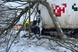 Lkw-Unfall auf glatter Fahrbahn, schwer beschädigtes Fahrzeug, Einsatzkräfte retten Fahrer.