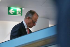 Friedrich Merz bei einer Rede in Davos, prominent im Vordergrund, Hintergrund unscharf.