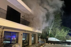 Brandrauch dringt aus einem Wohnhaus, Feuerwehr im Einsatz, verletzte Person, dramatische Rettungssituation.