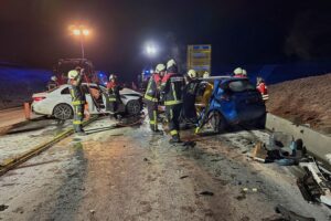 Unfallstelle mit Rettungskräften, Fahrzeugen und Beleuchtung, Einsatz der Feuerwehr sichtbar.