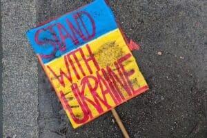Schild mit "Stand with Ukraine" auf Boden, symbolisiert Unterstützung für die Ukraine im Konflikt.