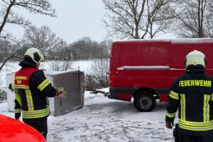 Umgestürzter Anhänger blockiert Straße, Feuerwehr im Einsatz, Fahrzeuge stehen in der Umgebung.