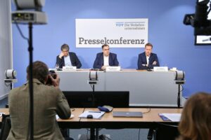 Ein Güterzug rollt durch eine Baustelle, umgeben von Baustellenfahrzeugen und Einschränkungen.