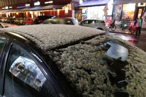 Schnee auf einem Autodach mit winterlichem, stürmischem Wetter im Hintergrund.