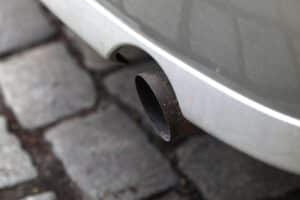Auspuff eines Fahrzeugs, der symbolisch für Treibhausgasemissionen und deren wirtschaftliche Auswirkungen steht.