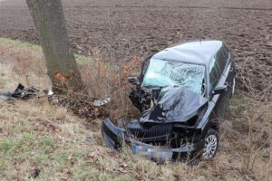 Verunfallter schwarzer PKW im Straßengraben, umgeben von Bäumen und der Unfallstelle.