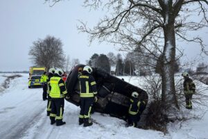 Ein Einsatzteam befreit Fahrer nach Unfall auf eisglatter Straße, umgeben von beschädigtem Auto.