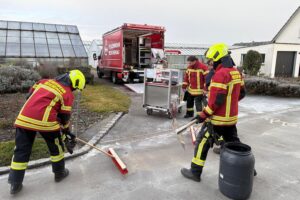 Feuerwehr behebt Dieselspur auf Straße, Einsatzkräfte mit Fahrzeug und Bindemittel im Einsatz.