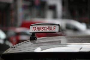 Fahrschüler mit Fahrlehrer, Verkehrsschilder, digitale Prüfungen, multikulturelle Umgebung, Führerschein-Entwicklung.