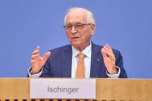 Wolfgang Ischinger spricht auf der Münchner Sicherheitskonferenz mit Friedrich Merz im Hintergrund.