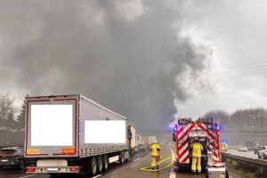 Brennender Lastwagen auf Autobahn, Feuerwehr im Einsatz, starke Rauchentwicklung, Verkehrsbehinderungen.