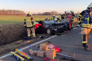 Verkehrsunfall mit Einsatzfahrzeugen, verletzter Person und umstehenden Helfern in einer ländlichen Umgebung.