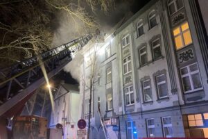 Drehleiter der Feuerwehr rettet Bewohner aus verrauchten Treppenhaus eines Mehrfamilienhauses während Brand.