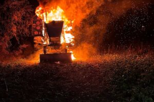 Brennender Traktor auf einem Feld, Feuerwehr löscht Flammen, Einsatzkräfte bei der Arbeit.