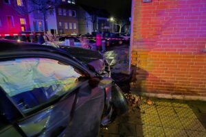 Verkehrsunfall mit zwei Pkw, Verletzte, beschädigte Hauswand und Feuerwehr im Einsatz.