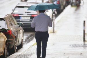 Mann mit Regenschirm unter dunklen Wolken, symbolisiert wechselhaftes, nasses Wetter in Rheinland-Pfalz.