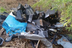 Illegal abgeladenes Auto im Wald, auffällige lila-violette Farbe, Umweltgefahr, Polizei ermittelt.