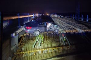 Ein Unfallfahrzeug auf einer Baustelle, umgeben von Bewehrungsstahl und Absperrungen.