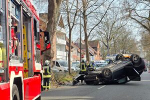 Verkehrsunfall mit umgekipptem Auto, Feuerwehr sichert Stelle, Rettungsdienst versorgt Fahrerin.
