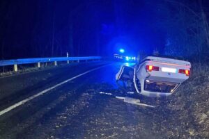 Unfallstelle mit überschlagenem BMW auf Landstraße, Rettungskräfte und Verkehrsabsperrung sichtbar.