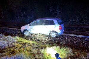 Verkehrsunfall mit schwer verletzter Beifahrerin, Polizei ermittelt, Auto auf Bahngleisen.