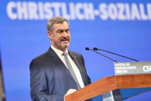 Markus Söder steht im Fokus, umgeben von politischen Symbolen und kritischen Stimmen seiner Partei.