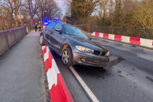 Unfallstelle mit beschädigtem Fahrzeug und Straßenleitwand, Einsatzkräfte bei der Bergung.
