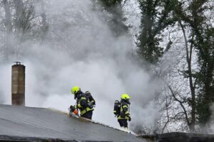 Feuerwehr mit Atemschutzgerät öffnet Dach eines Vereinsheims zur Brandbekämpfung.