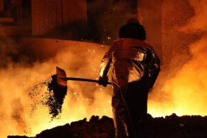 Stahlproduktion mit Maschinen, Arbeiter und Industrieanlagen; Symbol für Stellenabbau in der Metallbranche.