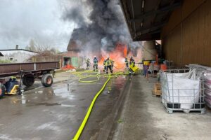 Großbrand in landwirtschaftlichem Betrieb; zerstörter Stall, Feuerwehr im Einsatz, Rauchwolke sichtbar.