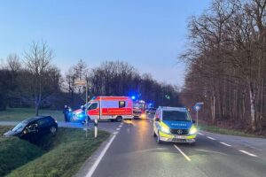 Ein Unfallwagen im Graben, Einsatzkräfte unterstützen verletzten Fahrer, Verkehrsabsperrung sichtbar.