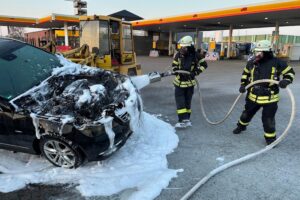 Feuerwehr löscht brennenden Mercedes-Benz Kombi auf Autohof, Fahrer erleidet leichte Verletzungen.