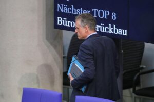 Ein besorgter Unternehmer betrachtet eine Anzeigetafel mit dem Thema "Bürokratieabbau" in Köln.