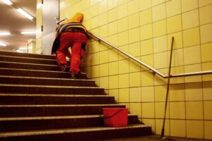 Reinigungskraft in U-Bahn-Station symbolisiert die Arbeitsrealität trotz steigender Mindestlöhne und Armutsgefahr.