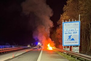 Brennendes Auto auf Autobahn, Feuerwehr im Einsatz, Unfallstelle gesichert, nächtliche Szene.