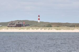 Sonniger Leuchtturm bei milder Temperatur, umgeben von wenigen Wolken und blauem Himmel.