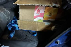 Zollbeamte beschlagnahmen unversteuerte E-Zigaretten aus einem Auto vor einem Kiosk.