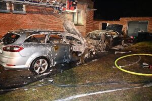 Zwei vollständig verbrannte Autos vor einem Mehrfamilienhaus in Stade, Feuerwehr im Einsatz.