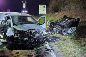 Schwerer Verkehrsunfall mit umgekipptem Fahrzeug, Feuerwehr im Einsatz, Einsatzkräfte und Absperrungen sichtbar.