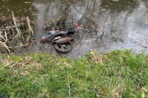 Ein alter Roller schwimmt in einem Teich, Polizei untersucht umweltschädliche Entsorgung.