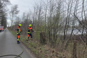 Feuerwehrleute löschen Böschungsbrand entlang Gleisen zwischen Bremen und Hamburg, Hubschrauber beobachtet aus der Luft.