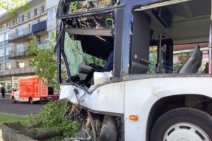 Verunglückter Bus auf der Straße, umgeben von Rettungskräften und beschädigten Bäumen.