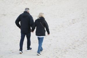 Paar am Strand spaziergehend, Symbol für gesellschaftliche Themen wie Gesundheit und Familie.