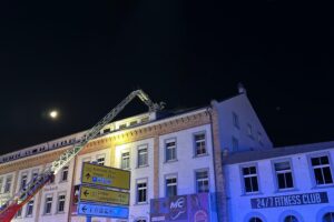 Feuerwehr im Einsatz bei Brand in dreistöckigem Geschäftsgebäude, Flammen und Rettungskräfte sichtbar.
